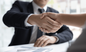 A private investigator in a black suit shakes hand with a new client to conclude the signing of a new contract.